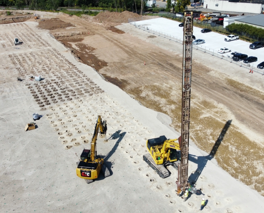 Aerial view of CNC Foundations performing aggregate pier installation at a construction site in Appleton, WI. A Komatsu excavator with a vibratory probe creates uniform pier locations for warehouse foundation stabilization.