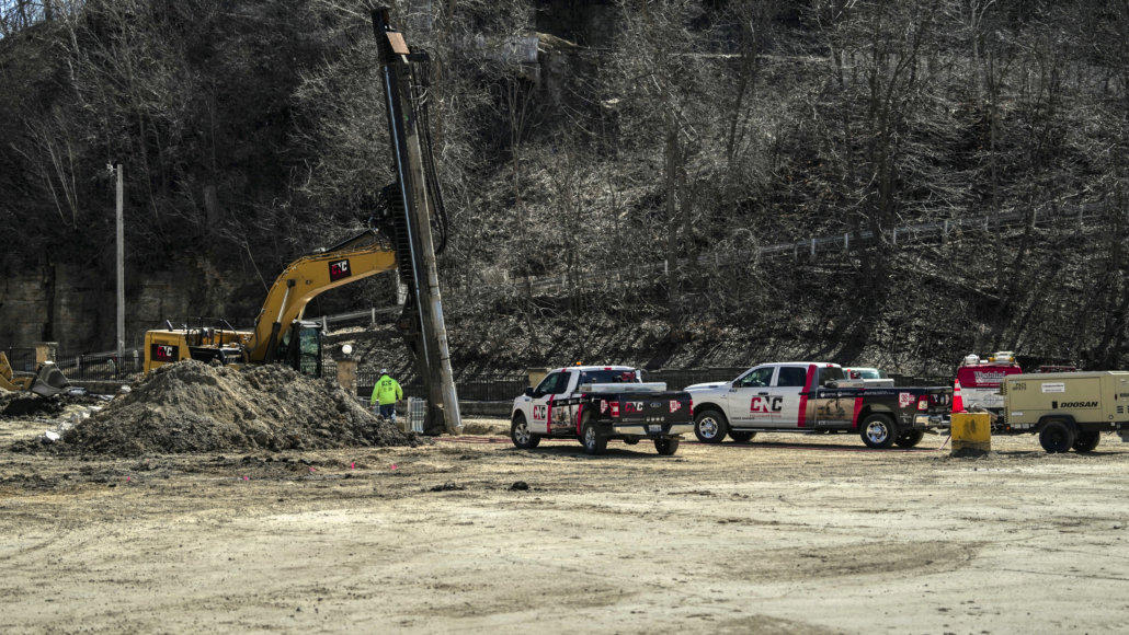 CNC Foundations equipment, including a drill rig and service trucks, staged at the Queen Marquette Casino site for ground improvement using grouted stone columns near a wooded bluff.